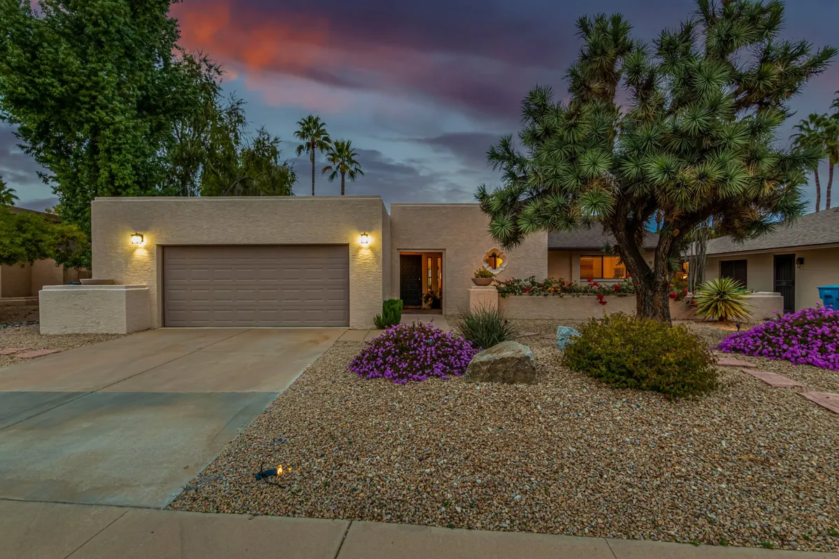This exterior image features a welcoming front entrance framed by mature palm trees, vibrant purple flowers, and a neat stone pathway. The lush landscaping and greenery convey a serene, tranquil setting, perfect for relaxation and outdoor enjoyment.