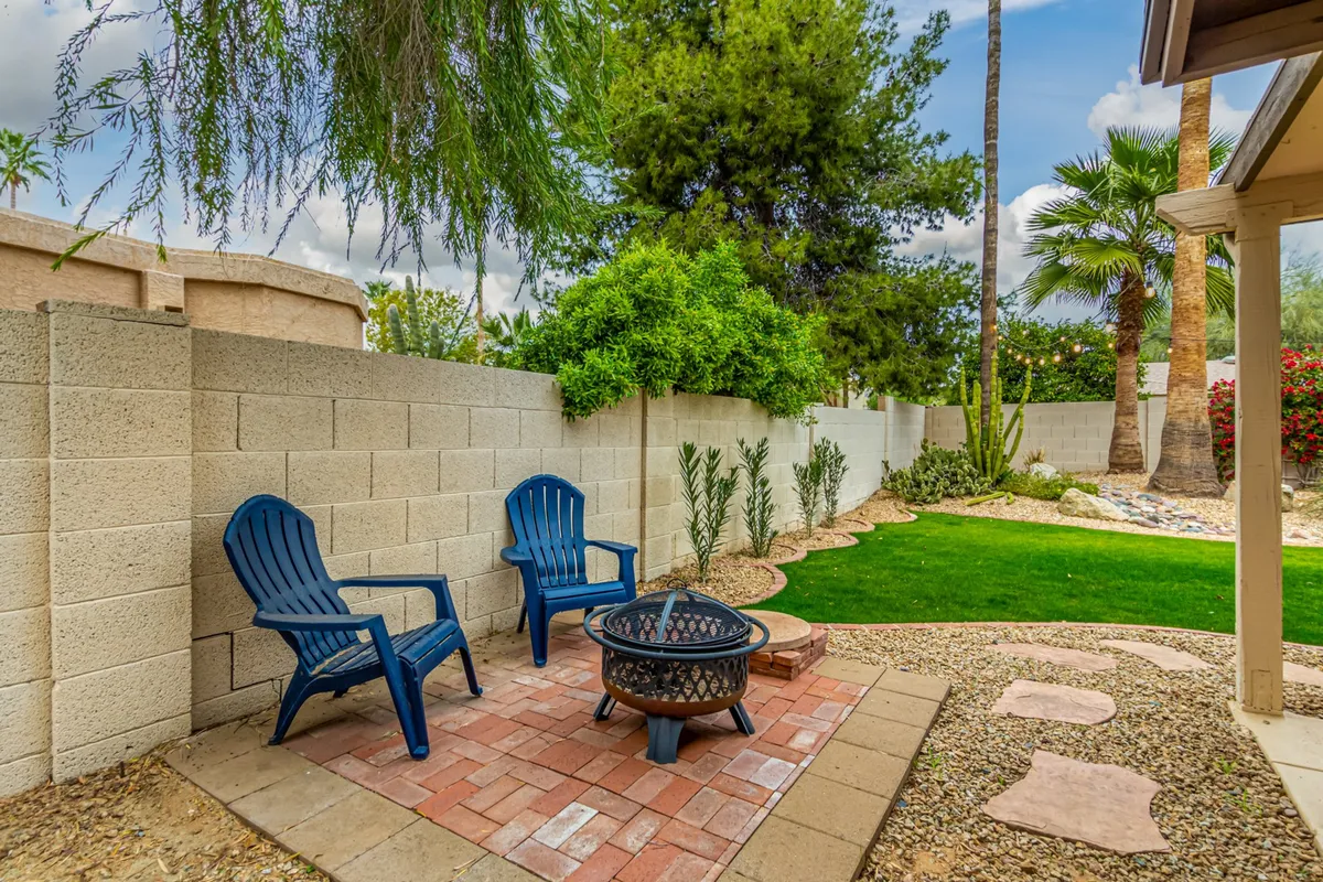 A cozy nighttime setup with blue chairs gathered around a glowing fire pit on green grass, backed by a textured wall. The ambiance is warm and tranquil, ideal for enjoying Arizona's evenings, sharing stories, or simply relaxing under the stars.