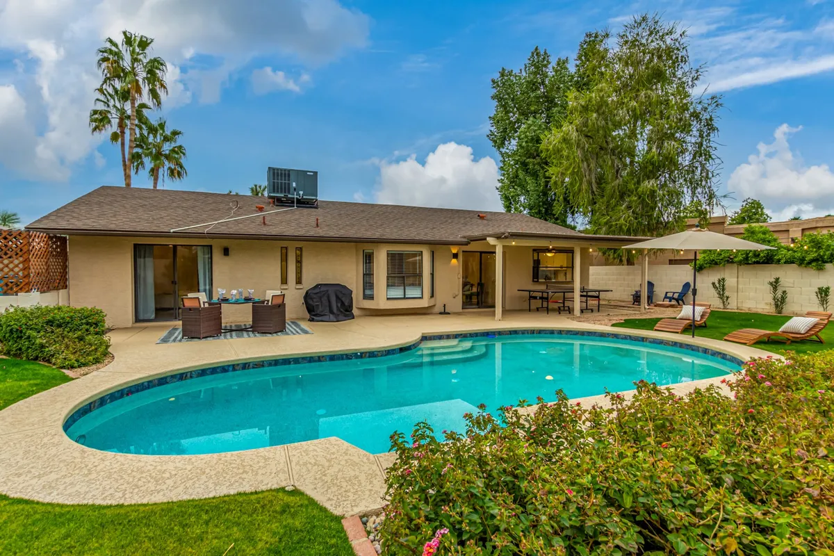 A vibrant backyard scene featuring a sparkling swimming pool surrounded by lush greenery and an inviting outdoor seating area. The space is perfect for family gatherings, with ample room for swimming, barbecuing, and relaxing in the Arizona sun. The overall mood is cheerful and lively, ideal for both daytime play and evening celebrations.