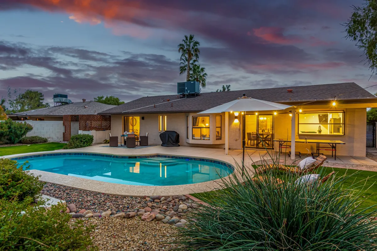 This inviting exterior scene showcases an attractive swimming pool, an outdoor seating area complete with a patio umbrella, and surrounds of landscaped garden. The space is designed for relaxing, entertaining, and enjoying celebrations with loved ones, evoking memorable summer nights and peaceful mornings alike.