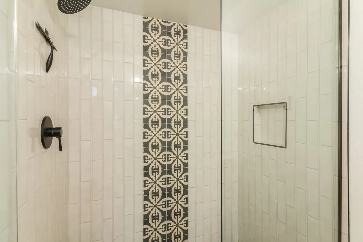 A walk-in shower with a striking black showerhead, a decorative tile strip, and a stylish glass enclosure. The design is both functional and visually appealing, perfect for refreshing after a day of adventure.