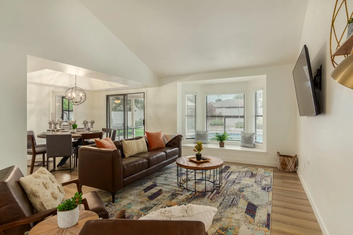 This inviting living room includes a plush leather sofa, a central coffee table, a cozy window seat overlooking the backyard, and tasteful decorative accents. The room is bathed in natural light, enhancing the sense of comfort and warmth ideal for relaxing or lively gatherings.